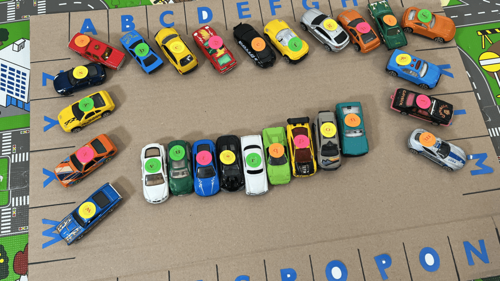 Alphabet Car Parking Game for Early Readers Angled view of toy vehicles with lowercase alphabet stickers parked on a handmade cardboard letter matching mat