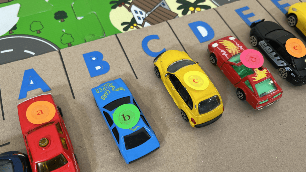 Alphabet Car Parking Game for Early Readers Close-up of toy vehicles with lowercase letter stickers parked in spaces A B C D E of an Alphabet Car Parking Game